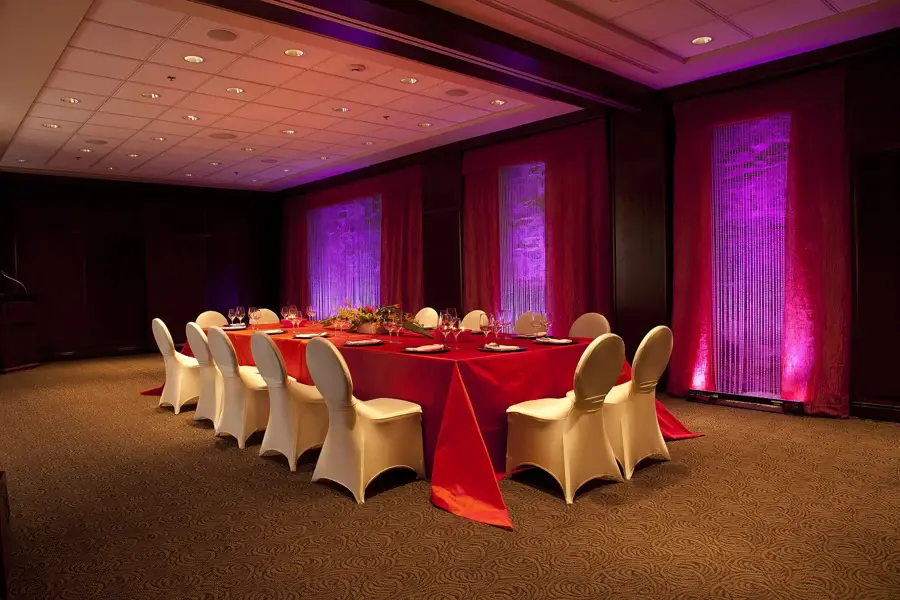 Salle de réception dressée avec une longue table nappée de rouge et des chaises housses blanches