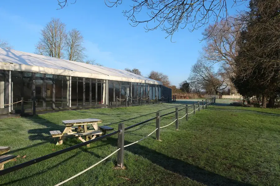 Grand chapiteau blanc de réception de mariage installé sur une pelouse, avec tables de pique-nique et arbres