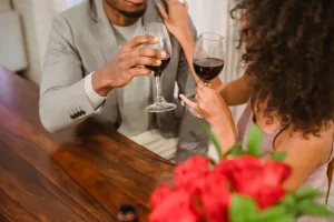 Couple trinquant au vin rouge à table, près d'un bouquet de roses