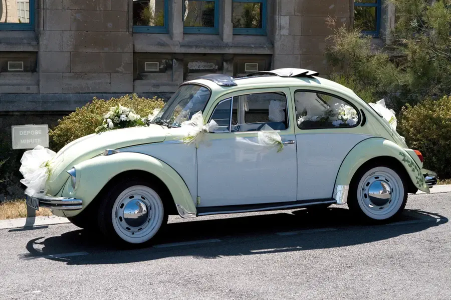 Voiture ancienne claire décorée de gros nœuds de tulle blanc devant un immeuble