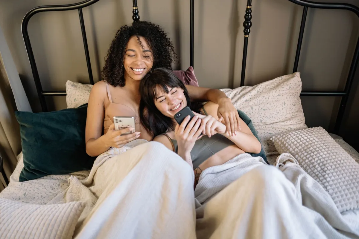 Couple allongé dans un lit, complice, chacun avec son téléphone en main