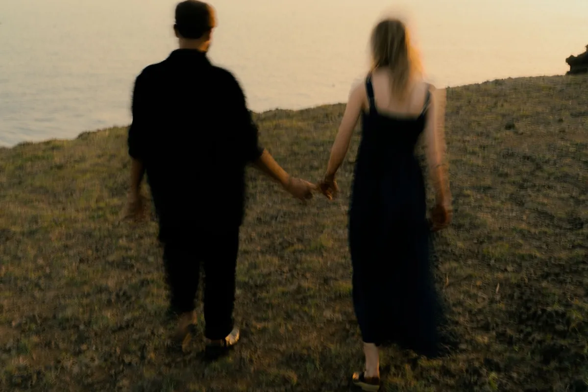 Couple marié marchant main dans la main au bord d'un lac au coucher du soleil